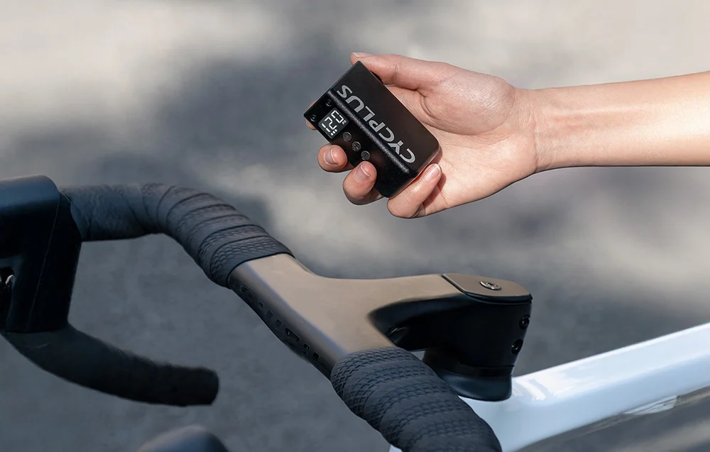 Dłoń trzymająca czarną mini pompkę Cycplus AS2 PRO nad ramą i kierownicą nowoczesnego roweru.